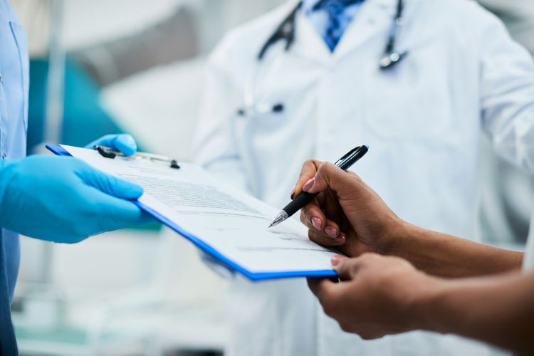 hands signing a document on a clipboard in a medical environment