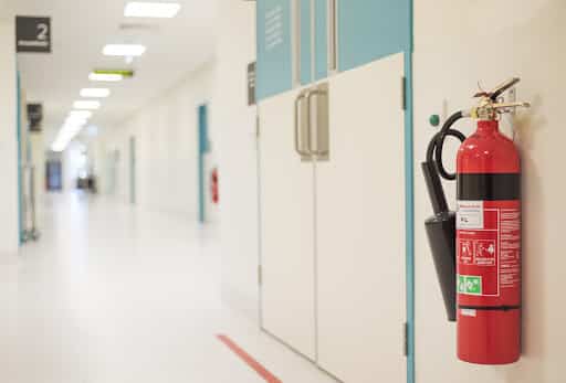 A fire hydrant is attached to a hospital wall. The hallway is empty and colored white.