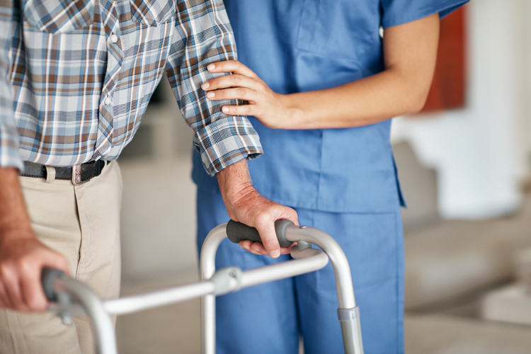 nurse helping older patient walk with walker