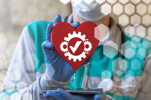 A healthcare professional reaches for a computer generated picture of a heart. They are wearing a mask and gloves and their face can not be seen.