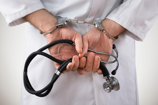 A doctor is pictured with his hands behind his back with handcuffs on. You cannot see his face.