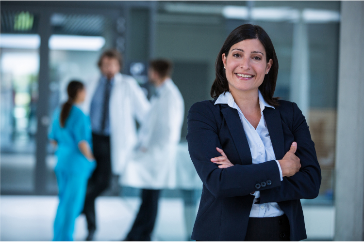 Confident female professional with certification in healthcare compliance smiling with medical staff in background