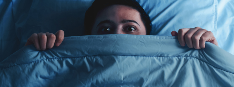 Person hiding under the covers of a bed