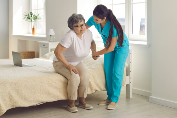Home health aide helping woman stand up from a bed